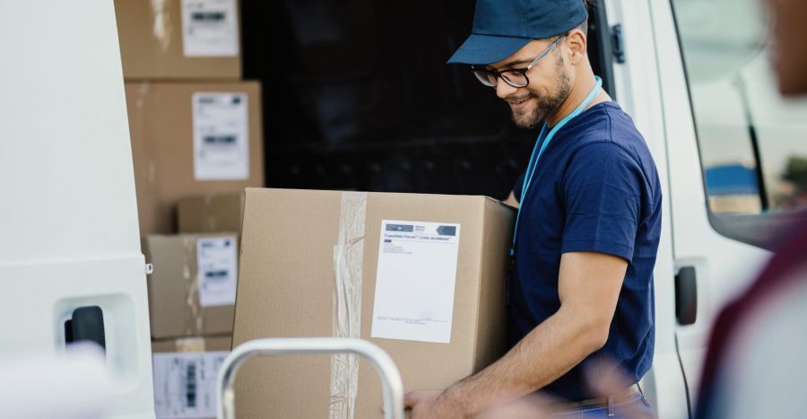 Young happy delivery man carrying cardboard box in a truck.